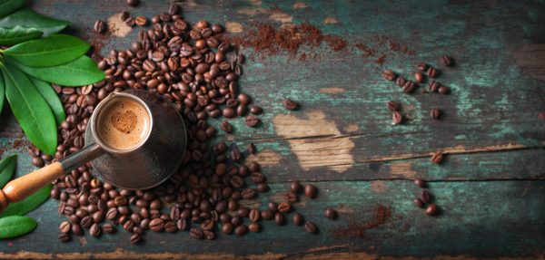 Hot coffee in a coffeepot or turk on a wooden background with coffee leaves and beans, horizontal with copy space. Top view